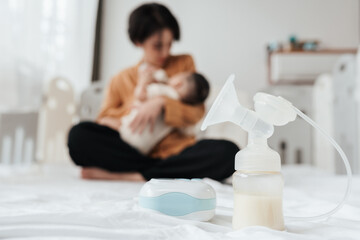Breast pump at foreground with mother lifting and playing newborn baby in background. mother's day concept.