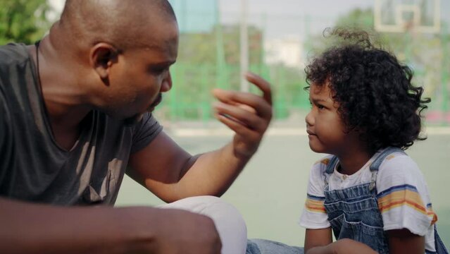 Father explaing basketball to son sitting at sports ground