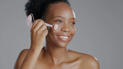Fotobehang Massagesalon Facial roller, woman and smile in face massage in skincare or beauty, health and wellness or dermatology. Happy black person, skin and cosmetics with glow, care and tool in studio by gray background