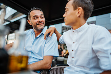 Handsome and happy father and his teenager son sitting in a restaurant and talking.