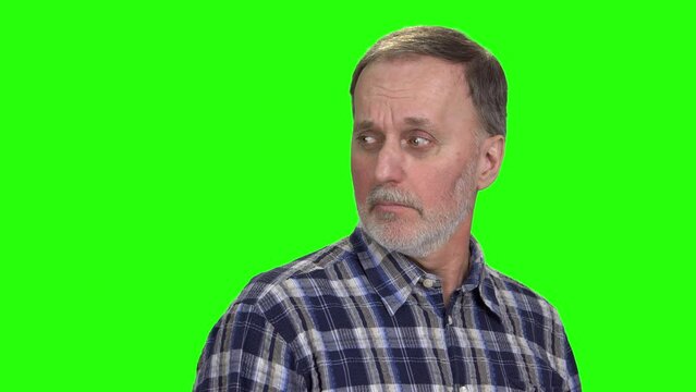 Portrait of aged caucasian man looking back contemptuously. Envy to someone. Isolated on green.