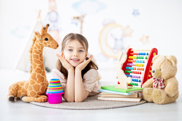 a small child girl plays with toys on a rug in a bright children's room building a pyramid lying on the floor, a smiling child at home playing, early preschool development