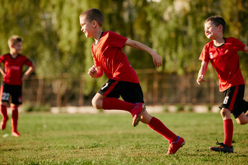 Obraz premium Full length side view portrait of kid, football player in sport uniform training, running at speed in motion before match on soccer field.