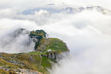 The plateau of Chlus with hiking paths at the Schaefler in Alpstein surrounded by the rising fog and with the peak Hoher Kasten at the far background.