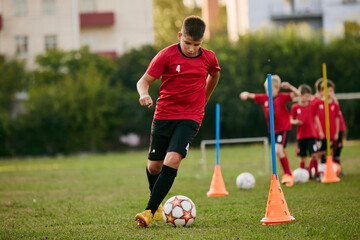 Close up portrait of school soccer player running dribbles ball on sport, football field on match...