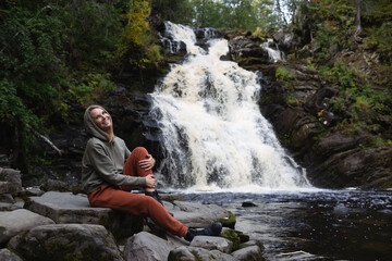 a young beautiful woman tourist sitting against the backdrop of a waterfall surrounded by forest