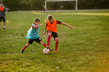 Boys running dribbling wearing sport uniform in team jersey and cleats. Kids play football on outdoor field. Children's school team.