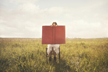 woman reading  a gigantic book that covers almost her entire face in the middle of a meadow