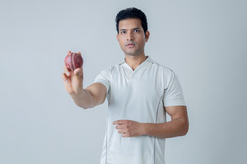 Portrait of Cricketer holding cricket boll in hand and looking towards the camera in aggression ,...
