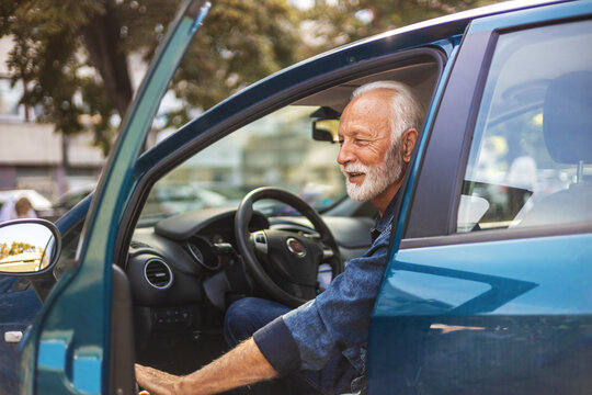 Happy senior man with blue shirt getting out of car in town. Smiling successful Caucasian businessman getting out of his car.
