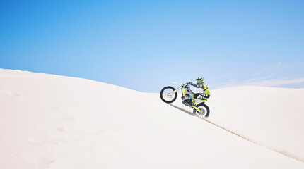 Man, driving and motorbike on sand with blue sky or sport, adventure and outdoor race in summer or...