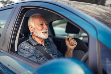 Close-up of happy senior man sitting in car in driver seat, driving.