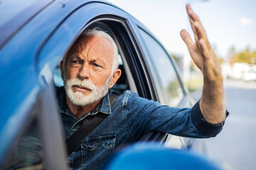 An irritated senior man driving a vehicle is expressing his road rage. Angry white hair man driving...