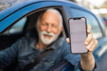 Cropped shot of a senior man driving a car and showing the smart phone with blanc screen.