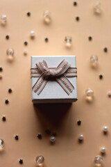 Small white present on neutral peachy background. Stars, pearls and beads in the background. Birthday or Christmas concept. Selective focus.