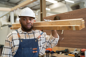 Male carpenter carrying piece of wood on his shoulder at wood processing plants. Male carpenter working at wood workshop. Joiner man carpenter at furniture workshop