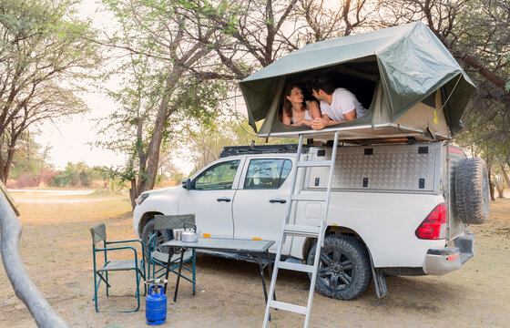 Young couple lying in a tent located on the roof of a pickup 4x4 car in a desert camp - Powered by Adobe