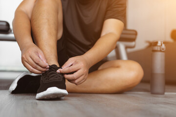 Close up fitness hand is tying shoelaces before workout in gym. Healthy man is getting ready to exercise.