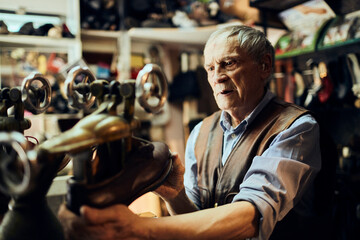 Senior male shoemaker restoring a shoe in his old workshop in the city