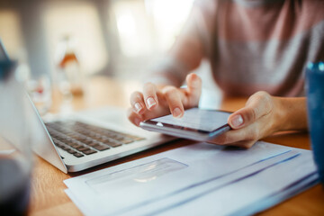 Young Caucasian woman using her smartphone and laptop at home