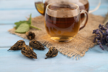 Red tea with herbs in glass on blue wooden. Side view, selective focus.