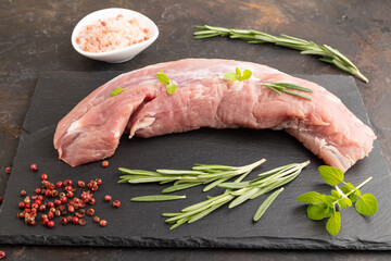 Raw pork meat with herbs and spices on slate cutting board on black concrete. Side view.