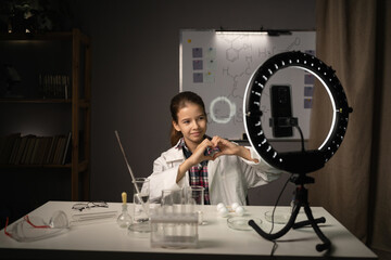 Teen Girl blogger researcher learning in experiment with test tubes in science chemistry class recording vlog. Girl student scientist with chemistry material in home lab showing heart gesture