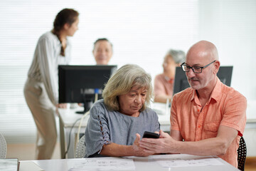 Obraz premium Teacher explaining senior woman how to send video messages on smartphone