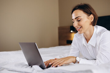 Business woman lying on bed and working on computer in a hotel room