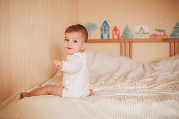 Fototapeta premium A little baby in a white bodysuit playing with lights sitting on a bed