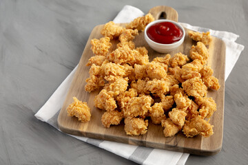 Homemade Crunchy Popcorn Chicken with Ketchup on a Board, side view.