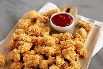 Homemade Crunchy Popcorn Chicken with Ketchup on a Board, side view.