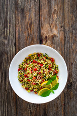 Tabbouleh salad - bulgur groats, tomatoes, cucumber, parsley, lemon, onion and fresh mint leaves on wooden background

