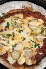 Food. Top view of a pizza with minced meat, tomato sauce, grilled cucumber, garlic aioli and chives, in a black pizza pan on the wooden table.
