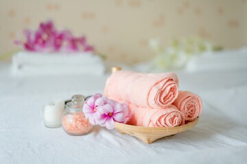 Peach towels with pink flowers and candles for relaxing spa massages and body treatments are placed on a council bed. Decorated with candles, spa stones and salts on wooden background. Copy space text