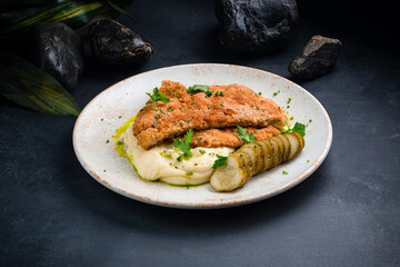 Fried breaded pork fillet with mashed potatoes, pickled cucumbers and herbs.