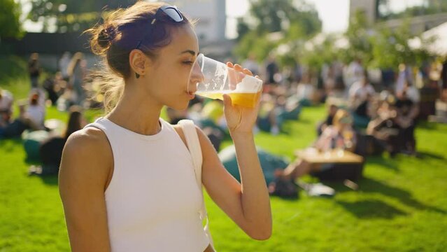 Portrait of beautiful young woman drinking beer and enjoying summer day. woman holding plastic glass with beer. party time outdoors. Happy hour, lunch break and youth concept