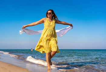 Fototapeta na wymiar Happy beautiful woman holding shawl walking on sunny beach 
