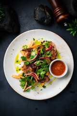 Pieces of fried pork fillet with French fries, onion, sauce and greens on dark background.