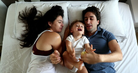 Cute family in bed with infant toddler. Father teasing baby son, top view