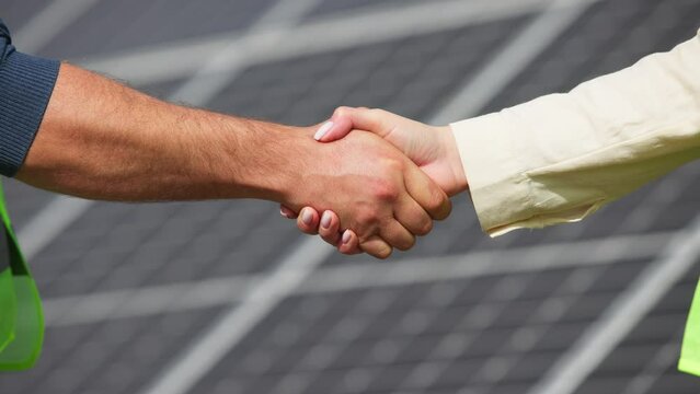 Close up of handshake on solar panel background outside. Female engineer shakes hands with partner in agreement.