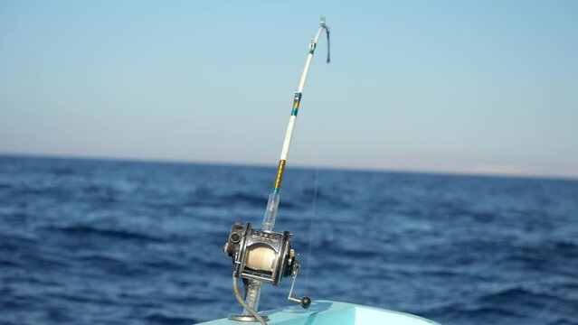 Bent fishing rod with electric fishing reel in holder on a motor boat in the sea