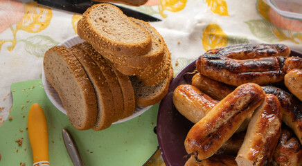 Slices of sesame bread, grilled sausages on a plate, rustic dinner on the table with a tablecloth