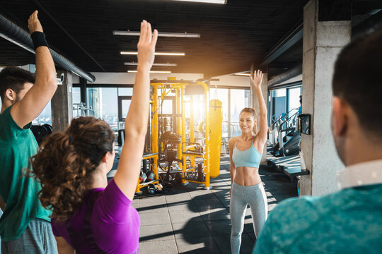 Group of athletic people exercising in a health club. Attractive female fitness instructor showing warming up exercises to her client in gym. Fit woman coach performing fitness exercises with a group.