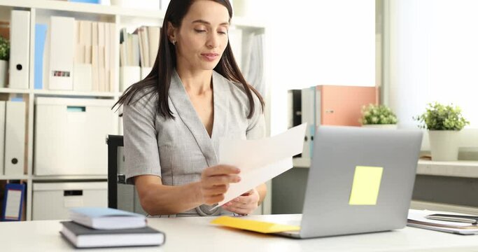 Woman employee opens envelope with awful news letter at wooden desk with laptop. Office worker looks at received letter with disappointment slow motion