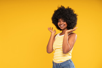 Charming girl looking and smiling to the camera. Attractive laughing african woman in casual clothes. Yellow pastel studio background.