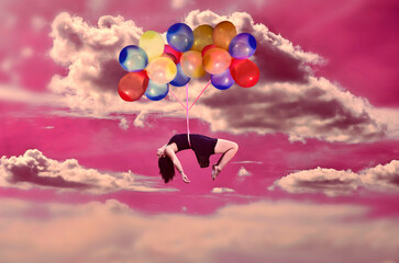 Mujer flotando con globos de colores en el cielo rosa con nubes de algodón - obrazy, fototapety, plakaty