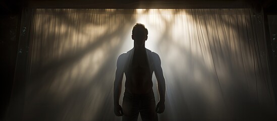 Silhouetted male figure posing behind a white curtain in an artistic photograph With copyspace for text