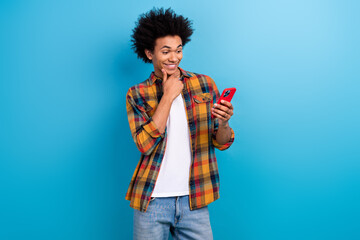 Photo of excited guy with perming coiffure dressed plaid shirt read sms on smartphone hand on chin isolated on blue color background