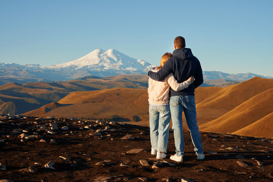 A young married couple welcomes the dawn in the mountains. A snow-covered volcano in the background. Copy space.